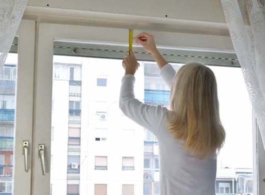 Blonde woman measuring and marking a position of a hole in order to install a blind. Residential building is in a background