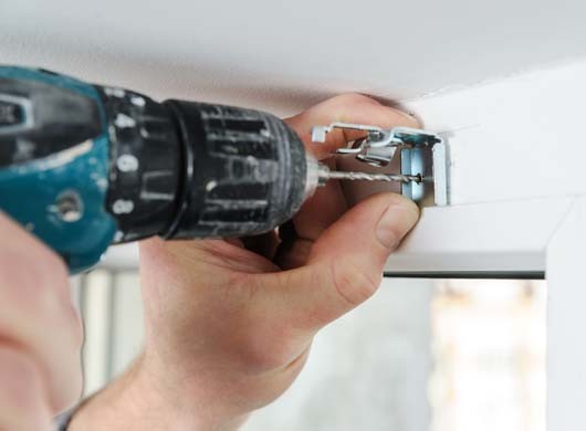 Man's hands  drill hole for fastening metal bracket that holds the jalousie.